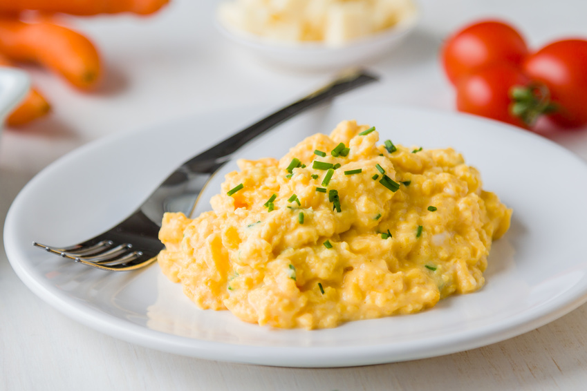 fresh scrambled eggs with green herbs on white plate with silver fork